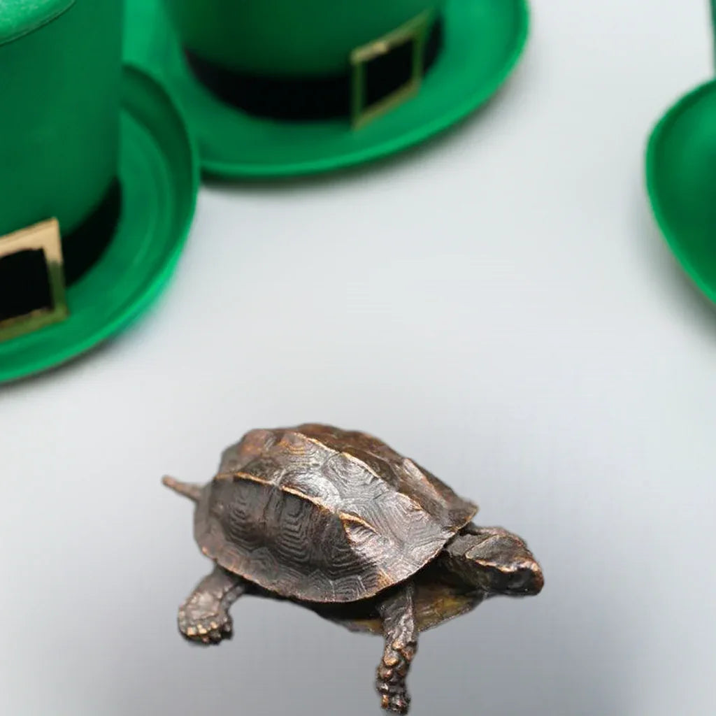 Vintage copper Feng Shui turtle statue placed near green hats, showcasing its use as a symbolic antique desk ornament and cultural decor piece.