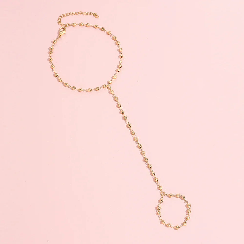 Flat lay of gold-plated faceted beads hand chain bracelet with finger ring, highlighting its minimalist goddess charm design.