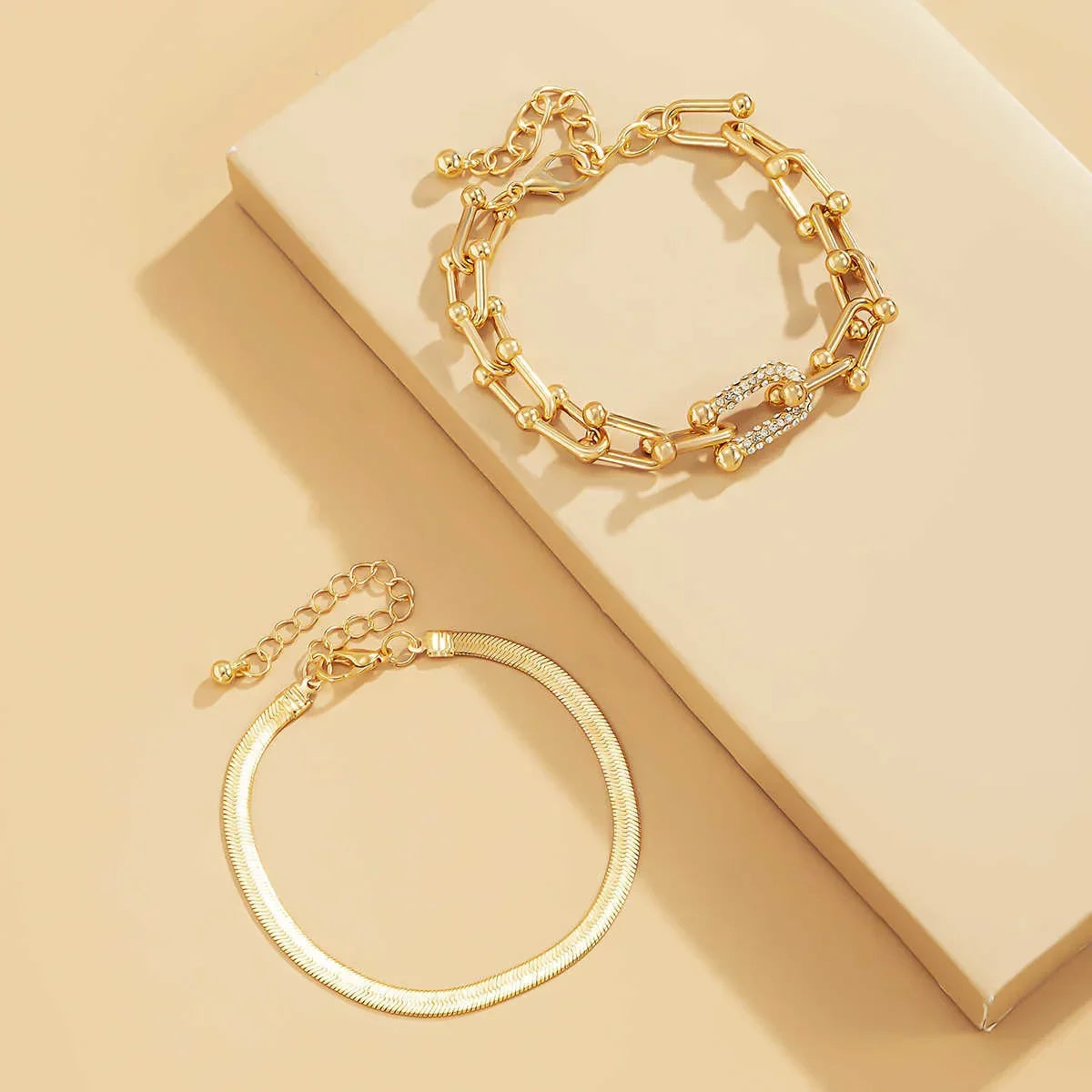 Trendy Geometric Bracelet Set – 2Pcs Gold U Chain displayed on beige surface, featuring textured and rhinestone-accented links.