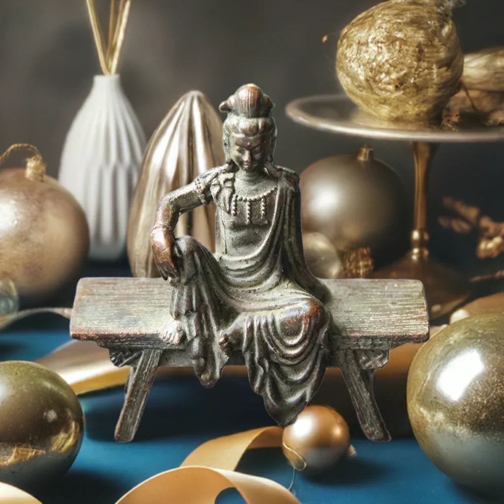 Bronze Guanyin Bodhisattva statue on bench with golden holiday decor, ideal for antique Feng Shui home styling.