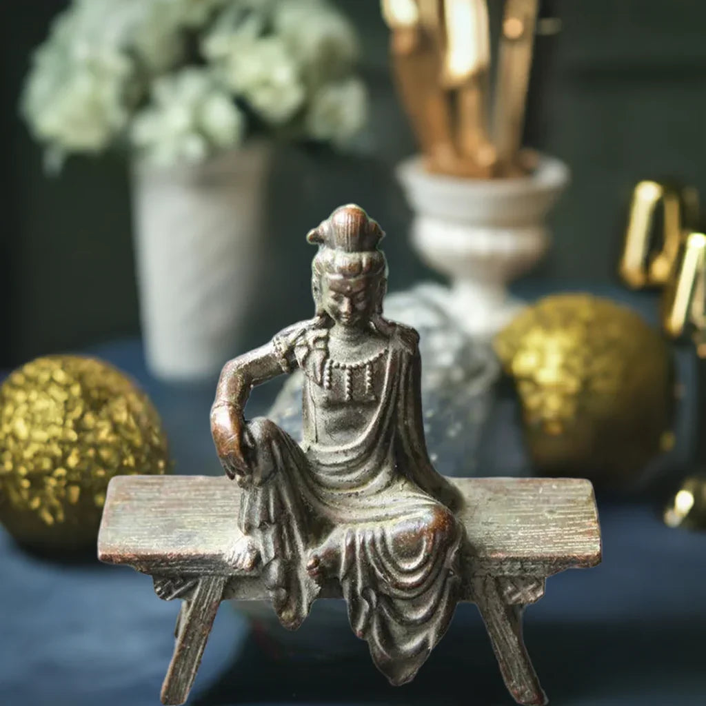 Decorative bronze Guanyin Bodhisattva statue on bench, surrounded by elegant ornaments for spiritual home decor ambiance.