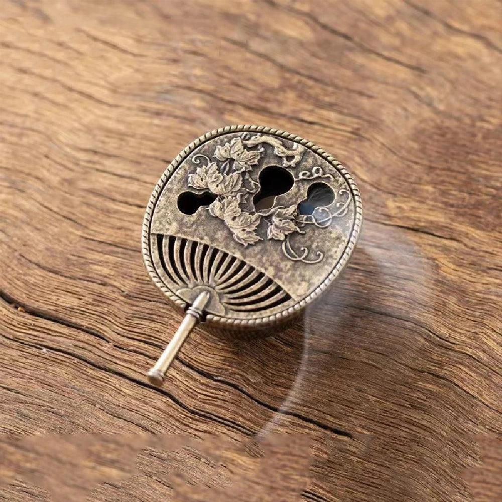 Decorative fan-shaped incense holder with floral engravings, releasing smoke for a calming Feng Shui and Zen atmosphere.