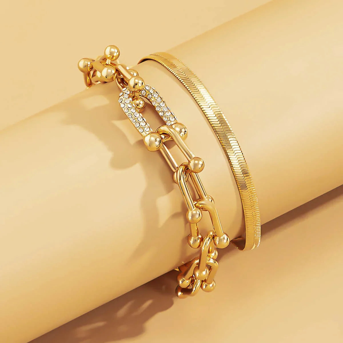 Close-up of Trendy Geometric Bracelet Set – 2Pcs Gold U Chain on beige roll, showing layered gold textures and rhinestone detail.