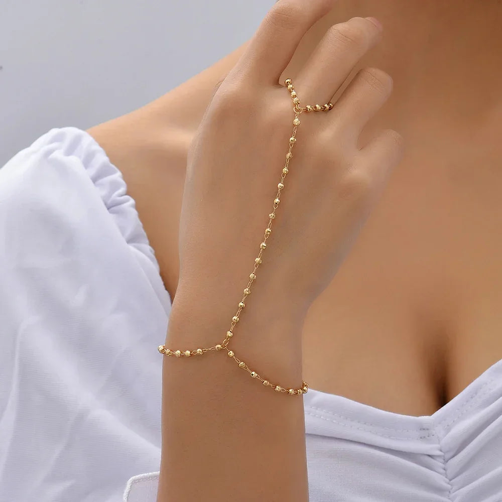 Minimalist gold-plated hand chain bracelet with faceted beads linked to finger ring, modeled on hand for elegant jewelry display.