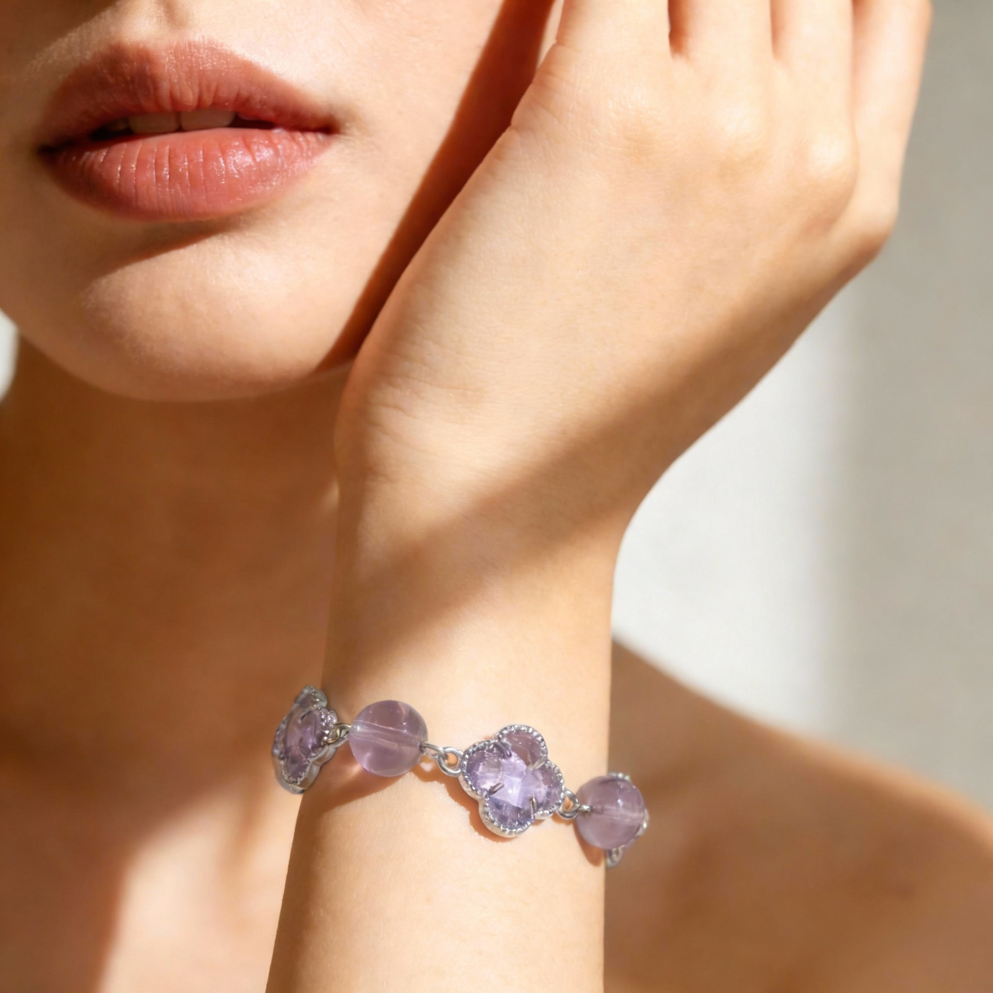 Close-up of a hand wearing a bracelet with purple gemstones, held near the face.